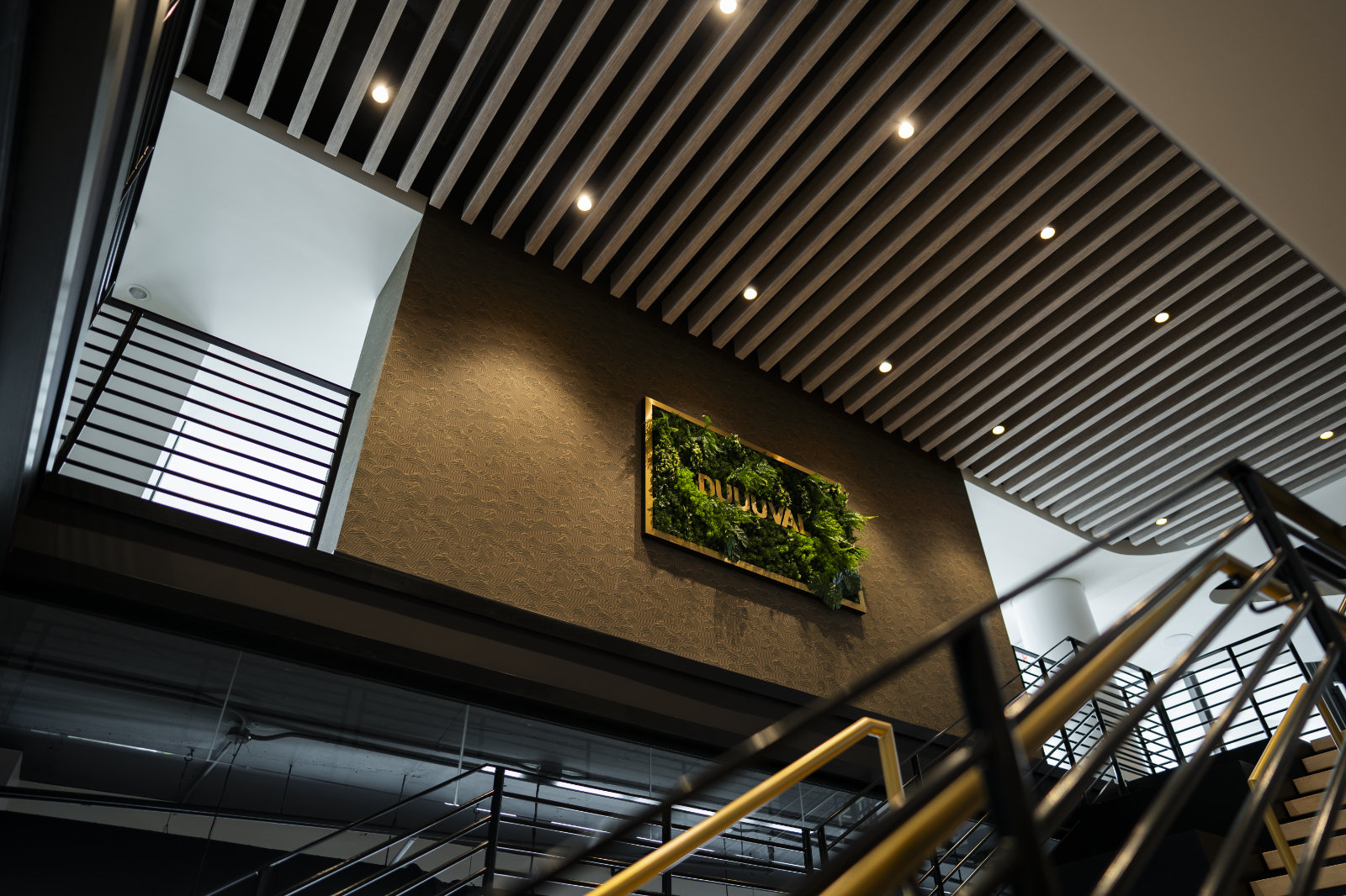 Upward angle shot of staircase reveals wood slats on ceiling and wall sign with foliage.