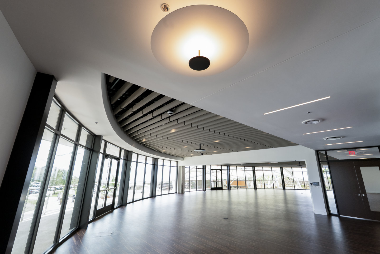 Low angle wide shot reveals open wooden floor, wooden slatted ceiling and curved exterior wall made entirely of windows.