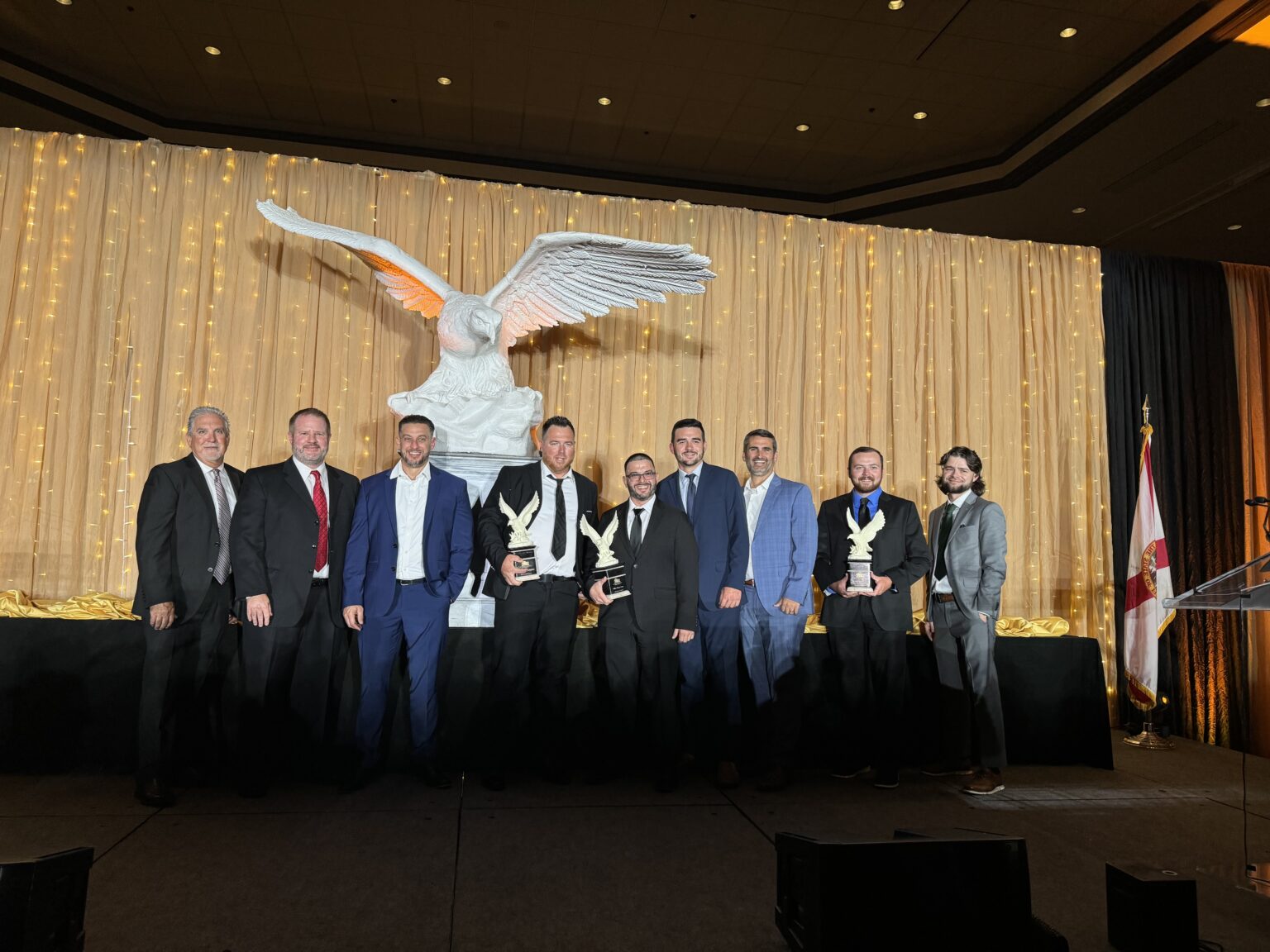 Leadership team holding eagle trophies standing in front of statue.