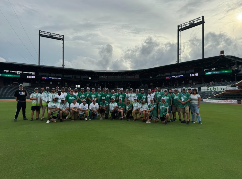 Leaders at Miller Electric pose for a group picture on a baseball field.