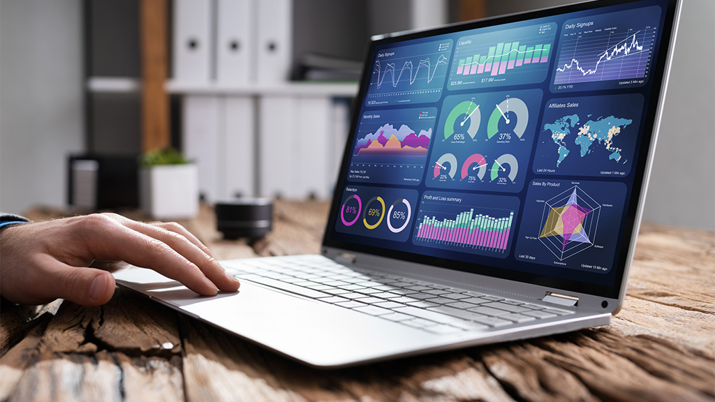 Laptop on a desk with a dashboard of various metrics on it.