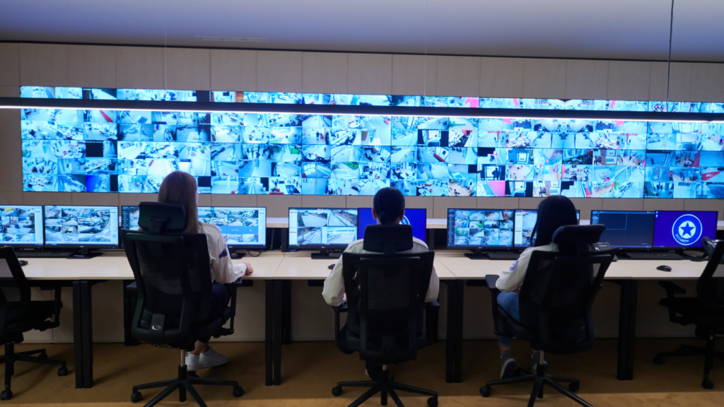 Team of people sitting at a desk looking at a wall of monitors that have feeds from security cameras