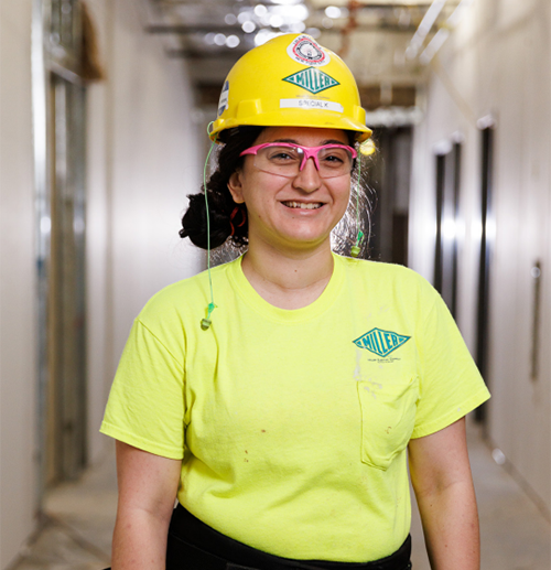 Girl in yellow hard hat and pink safety glasses smiles