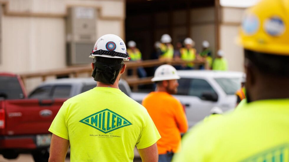 Workers in safety gear with Miller Electric's logo on it.