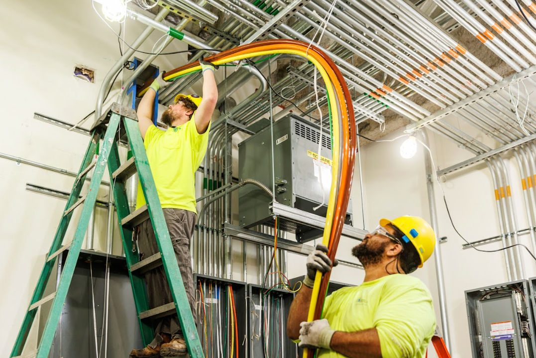 Apprentice and Journeyman electrician working on pulling cable. One is on a ladder.